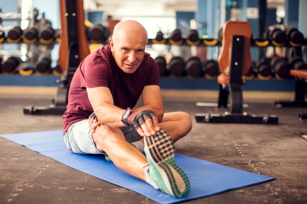 Older man stretching on a mat in a gym
